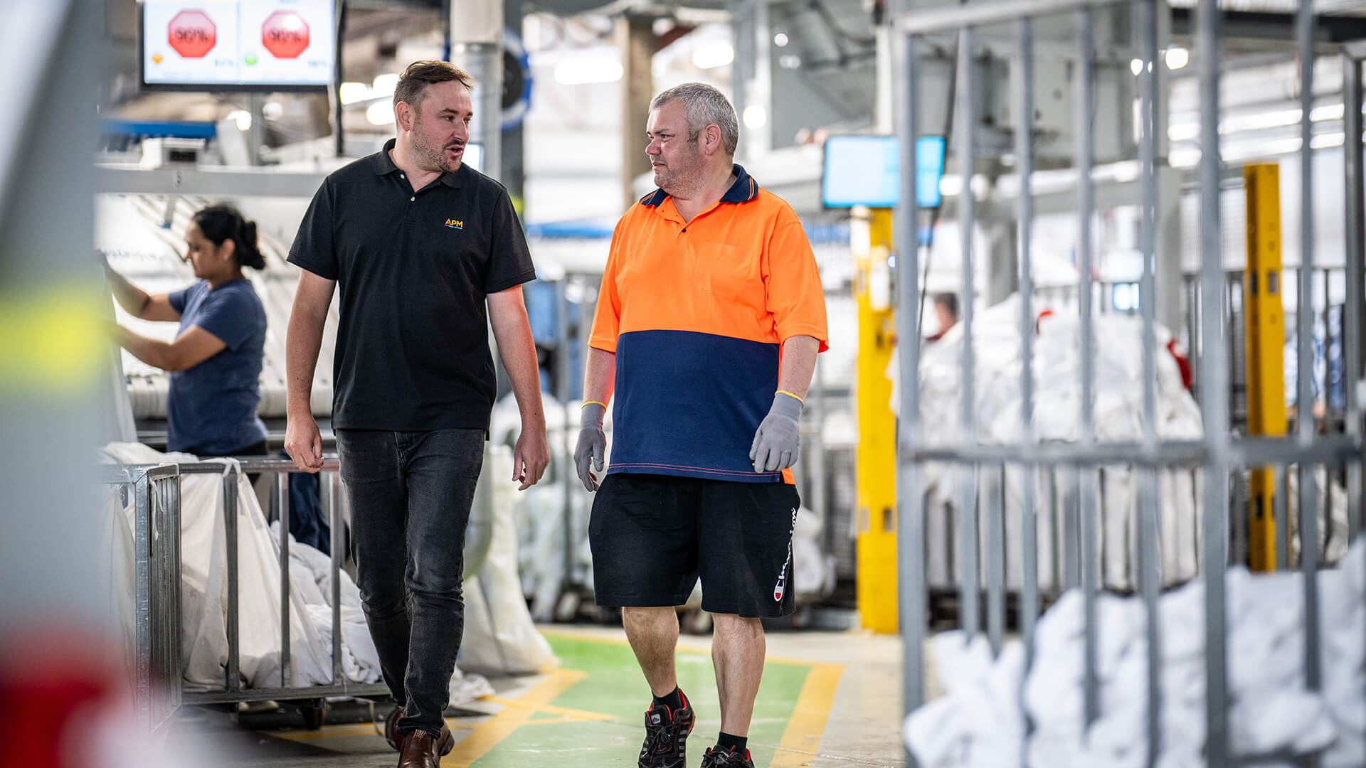 APM consultant walks through a factory with a worker in a high vis top